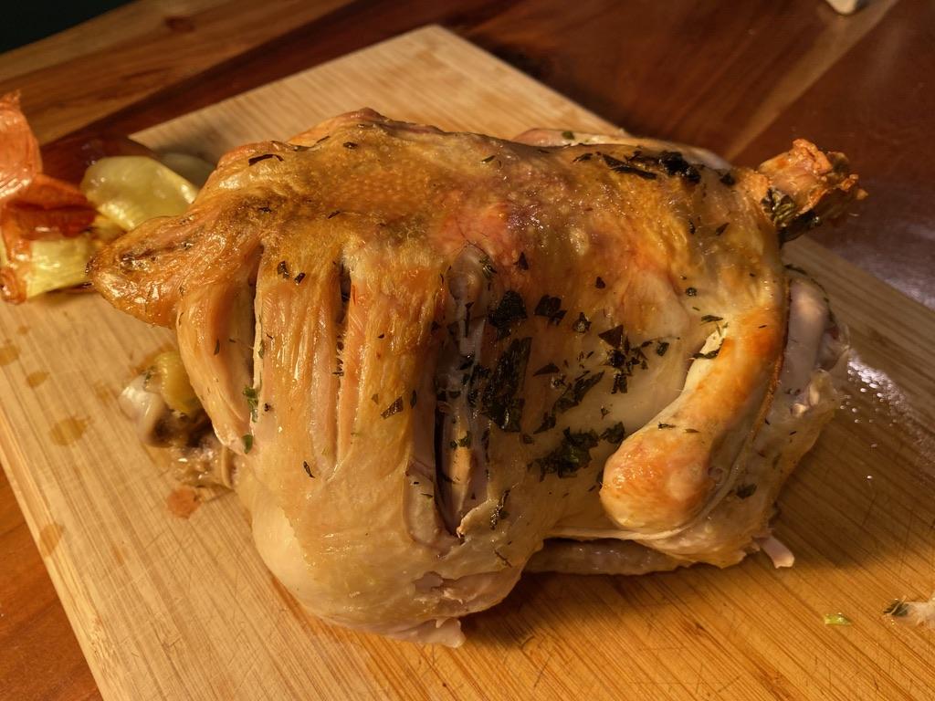 Image of a cooked chicken resting on a wooden cutting board.