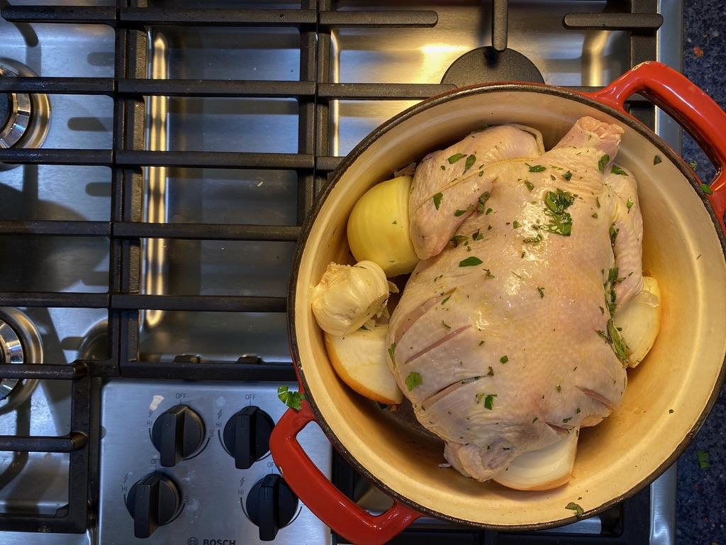 Image of a raw chicken, lemon, garlic, and onion in a pot on a stovetop.