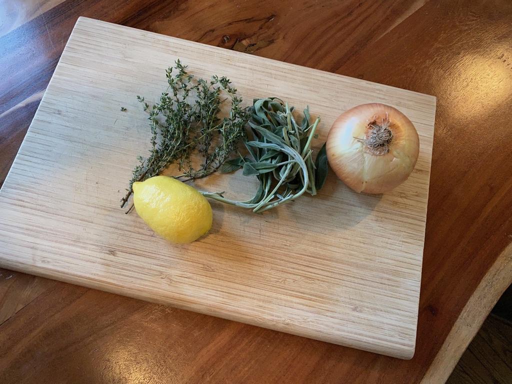 Image of herbs, a lemon, and an onion sitting on a wooden cutting board.